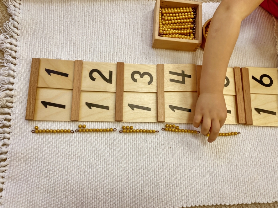 child matches beads to numbers on wooden flash cards at Montessori school