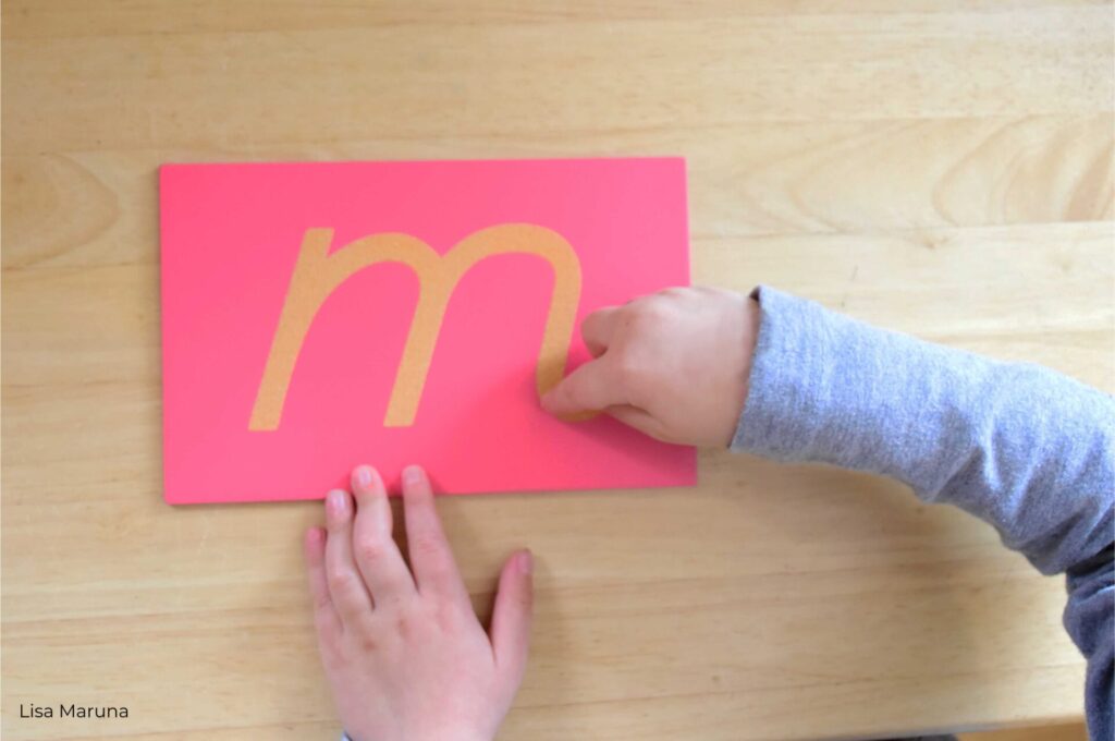 child traces letter M with finger at Montessori school by Lisa Maruna
